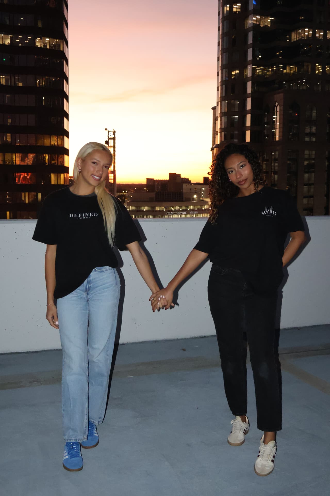 Two models in Defined Gym Brand tees on a rooftop as the sun sets behind the skyline